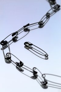 Image shows safety pins in a chain and one safety pin standalone in the middle.