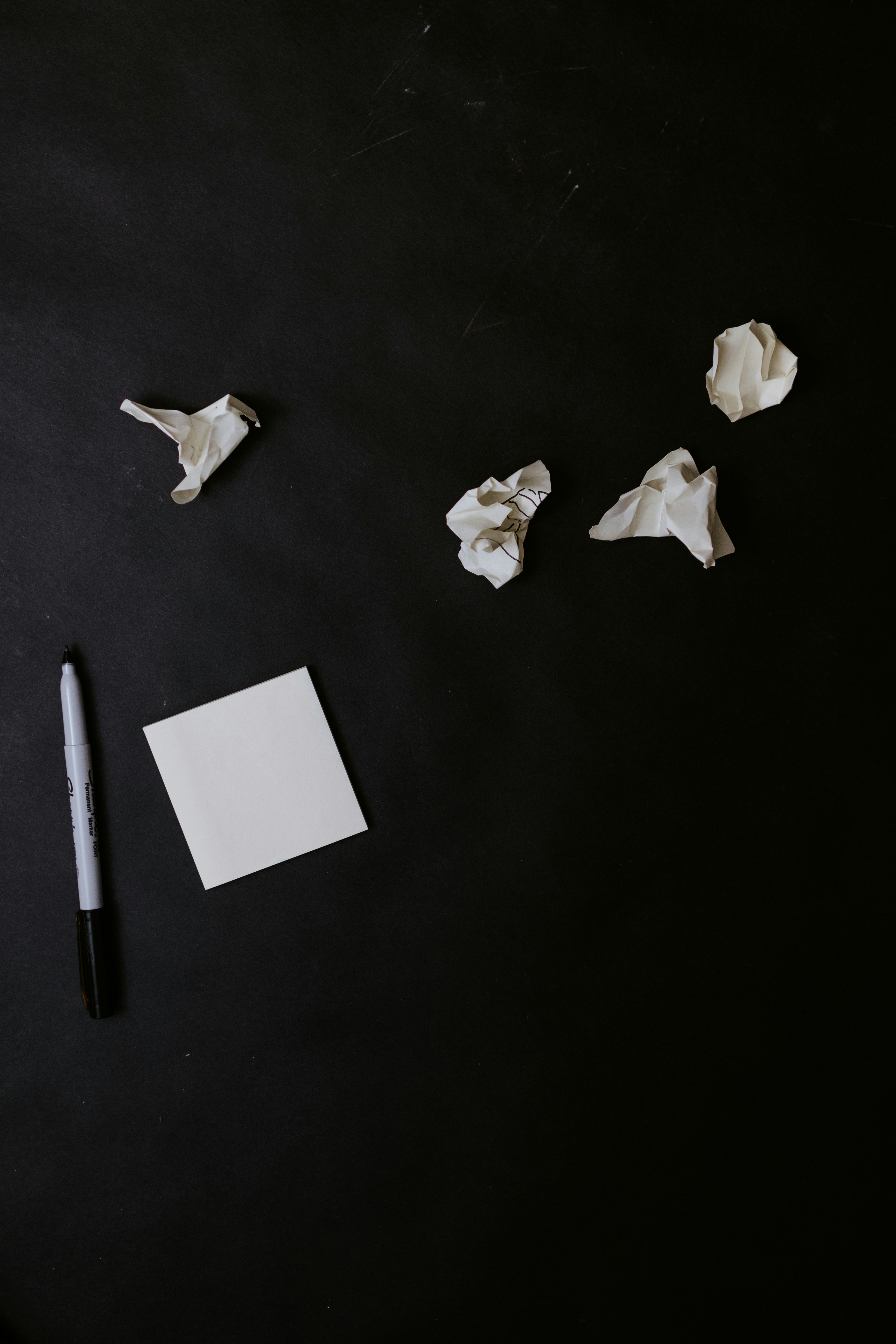 Image shows a black background with white post it nores and a black and white pen. There are crumpled bits of paper above that.