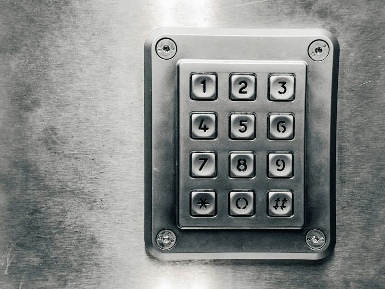 A grey metal pin pad with numbers 0 to 9 is secured to a grey wall.