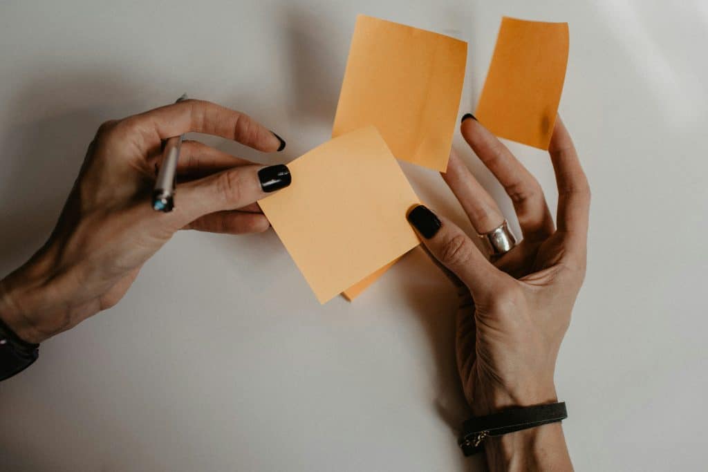 Does Your Dspt Submission Require An External Audit? 4 Two hands hold orange paper post-it notes. The left hand has a pen between the fingers. The fingers have black nail varnish on.