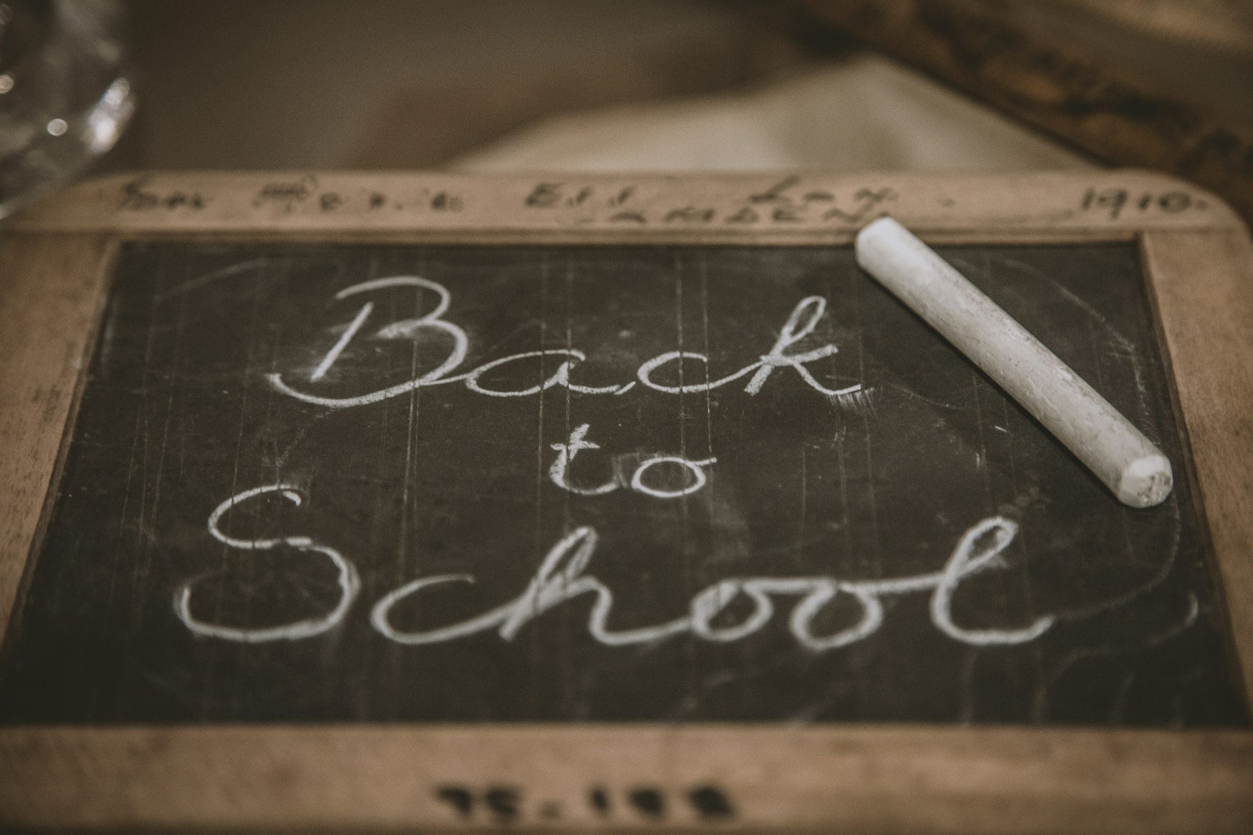 A chalkboard has a piece of white chalk resting against it. The words 'back to school' are written in italics on the chalkboard.