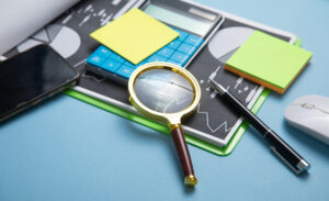 Image shows an example of items typically used for an DSPT audit, such as post it notes, pen, magnifying glass and paper.
