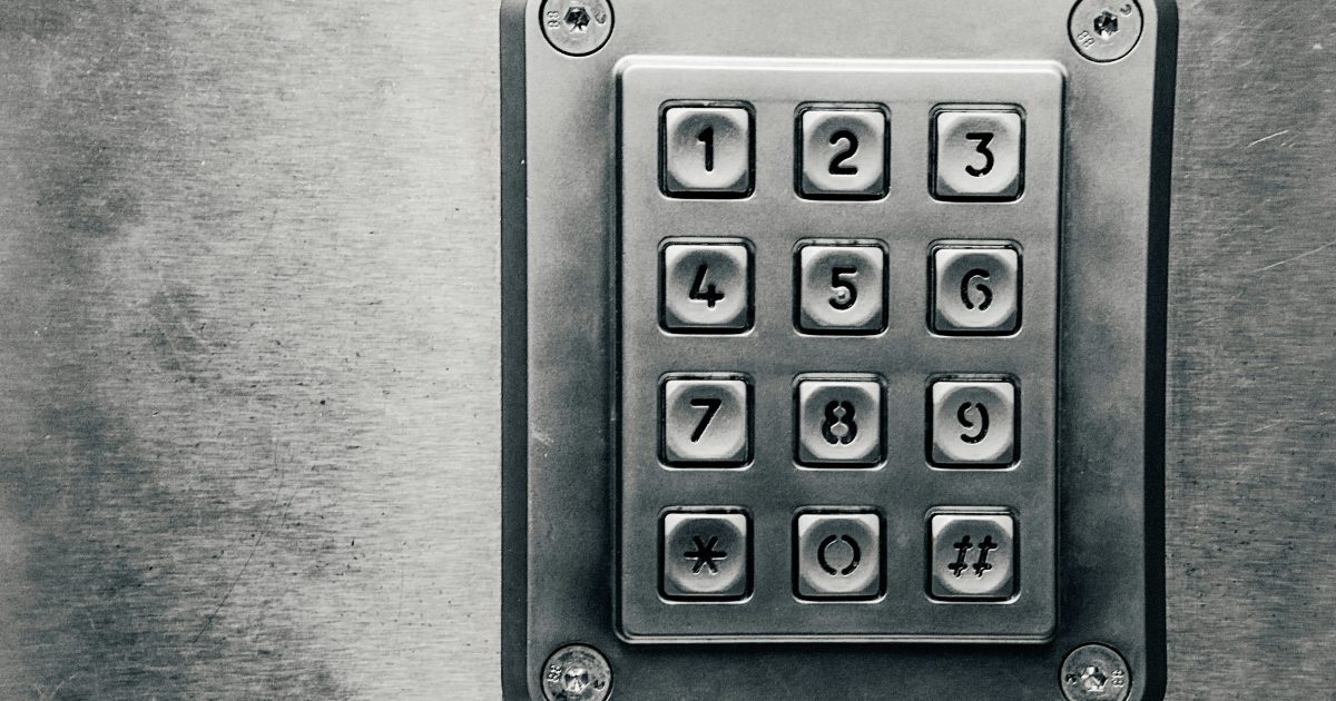 A grey metal pin pad with numbers 0 to 9 is secured to a grey wall.